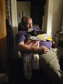 a man in a purple shirt is laying down with a cat on his lap