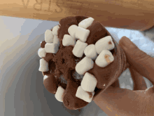 a person is holding a chocolate ice cream cone with marshmallows on it