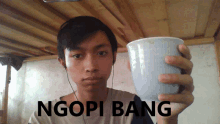 a young man holding a cup that says ngopi bang on the bottom