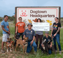 a group of people and their dogs pose in front of a dogtown headquarters sign