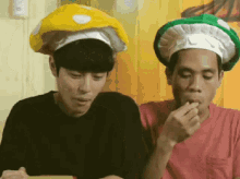 two men wearing chef hats are eating food together