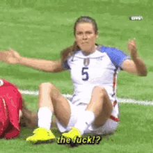 a female soccer player with the number 5 on her jersey sits on the field giving the middle finger .