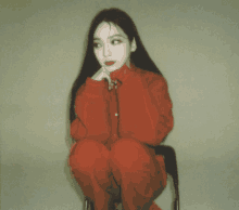 a woman in a red jumpsuit sits on a chair with her legs crossed