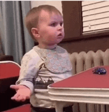 a baby is sitting at a table with a toy car .