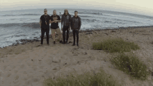 a group of men standing on a beach with one wearing a shirt that says ' a ' on the front