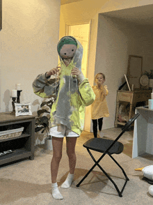 a woman in a tie dye hoodie stands in front of a chair