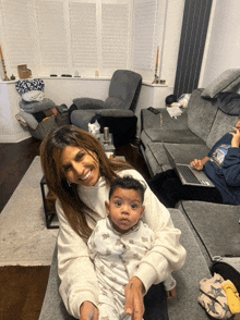 a woman holding a baby in a living room with a man using a laptop