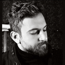 a man with a beard is wearing a black turtleneck and a black jacket