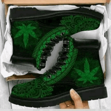 a pair of green and black boots with a marijuana leaf design on them are sitting in a box .