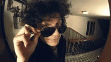 a man with curly hair wearing sunglasses is looking through a door .