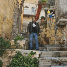 a man wearing a black shirt with a skull on it stands on a set of stairs in front of a building