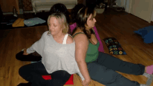 two women are sitting back to back on a wood floor