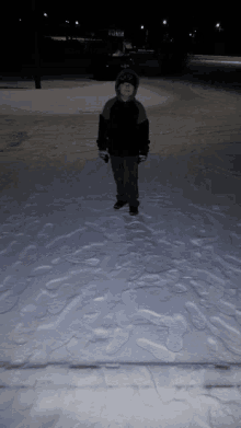 a young boy in a black jacket stands in the snow in front of a sign that says ' ice rink '