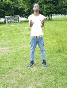 a young man in a white shirt and jeans is standing in a grassy field .