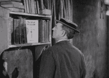 a man in a hat is standing in front of a bookshelf with a book titled the art of foolish .