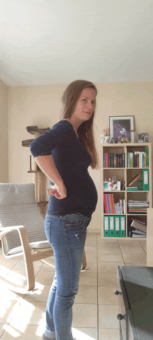 a pregnant woman stands in front of a bookshelf with binders on it