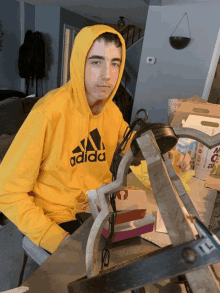 a young man wearing a yellow adidas hoodie sits at a desk