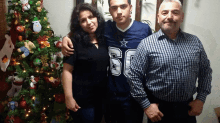 a man wearing a jersey with the number 60 on it poses with his parents in front of a christmas tree