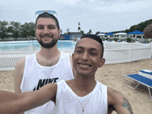 a man wearing a nike tank top stands next to another man on the beach