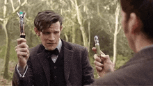 a man in a suit and bow tie is holding a pair of sonic screwdrivers in his hands .