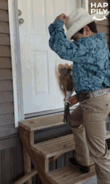 a man wearing a cowboy hat is holding a bouquet of flowers in front of a door that says hap pily