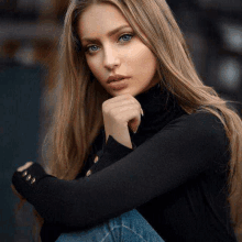 a woman with long blonde hair and blue eyes is wearing a black turtleneck sweater and jeans .