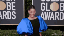 a woman in a black dress with blue puffed sleeves is standing in front of a sign that says be glob award