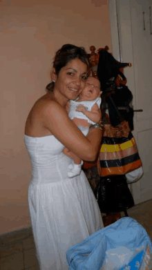 a woman in a white dress holds a baby