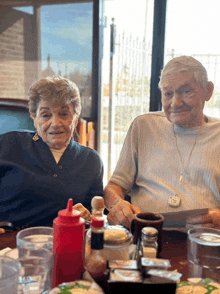 a man and a woman are sitting at a table with a ketchup bottle on it