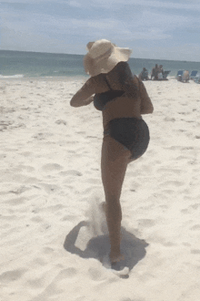 a woman in a bikini and a hat is walking on a beach