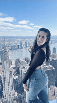 a woman in a black top and blue jeans stands in front of the empire state building in new york city