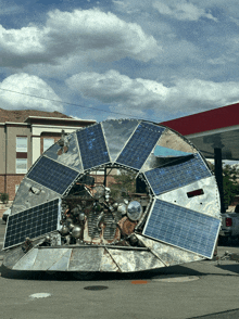 a large circular object with solar panels on it is parked in front of a gas station