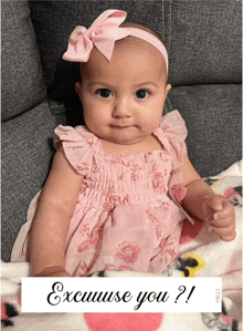 a baby in a pink dress is sitting on a couch next to a sign that says excuse you ?