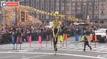 a large skeleton is walking down a street in front of a crowd with a sign that says en vivo