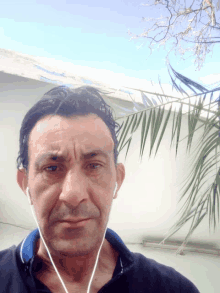 a man wearing ear buds looks at the camera in front of a palm tree