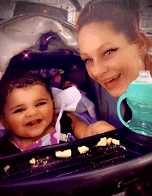 a woman holding a baby in a stroller with a tommee tippee cup in front of her