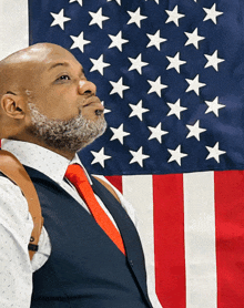 a bald man in a suit and tie stands in front of an american flag