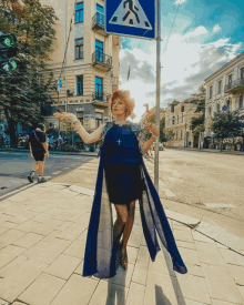 a woman in a blue dress stands in front of a blue sign that says crosswalk