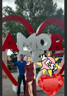 a man and a woman standing in front of a large red heart that says amor