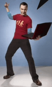 a man in a red shirt is holding a laptop and pointing