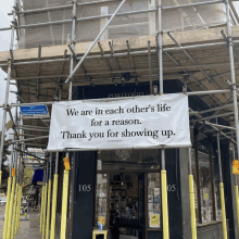 a white banner hangs from a scaffolding outside a store that says we are in each other 's life for a reason