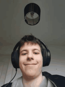 a young man wearing headphones is smiling and looking at the camera while a lamp shade is hanging from the ceiling .