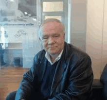 a man in a leather jacket is sitting in a chair in front of a glass door .