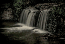 a waterfall is surrounded by rocks and trees in the dark