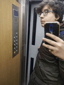 a boy taking a picture of himself in an elevator with a phone that says ' samsung ' on it