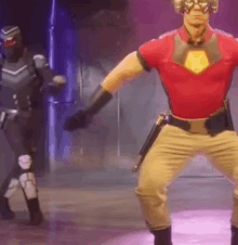 a man in a superhero costume is dancing on a stage with another man in a black suit .