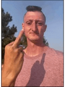 a man with a mohawk is giving the middle finger and his shadow is visible .