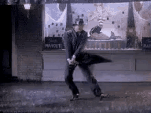 a man in a hat is dancing in the rain with an umbrella in front of a store with a sign that says marquette