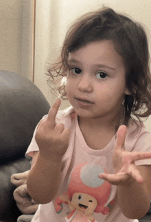 a little girl wearing a pink shirt with a mushroom on it giving the middle finger