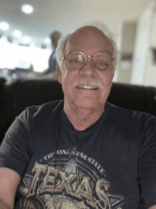 a man wearing glasses and a texas shirt smiles